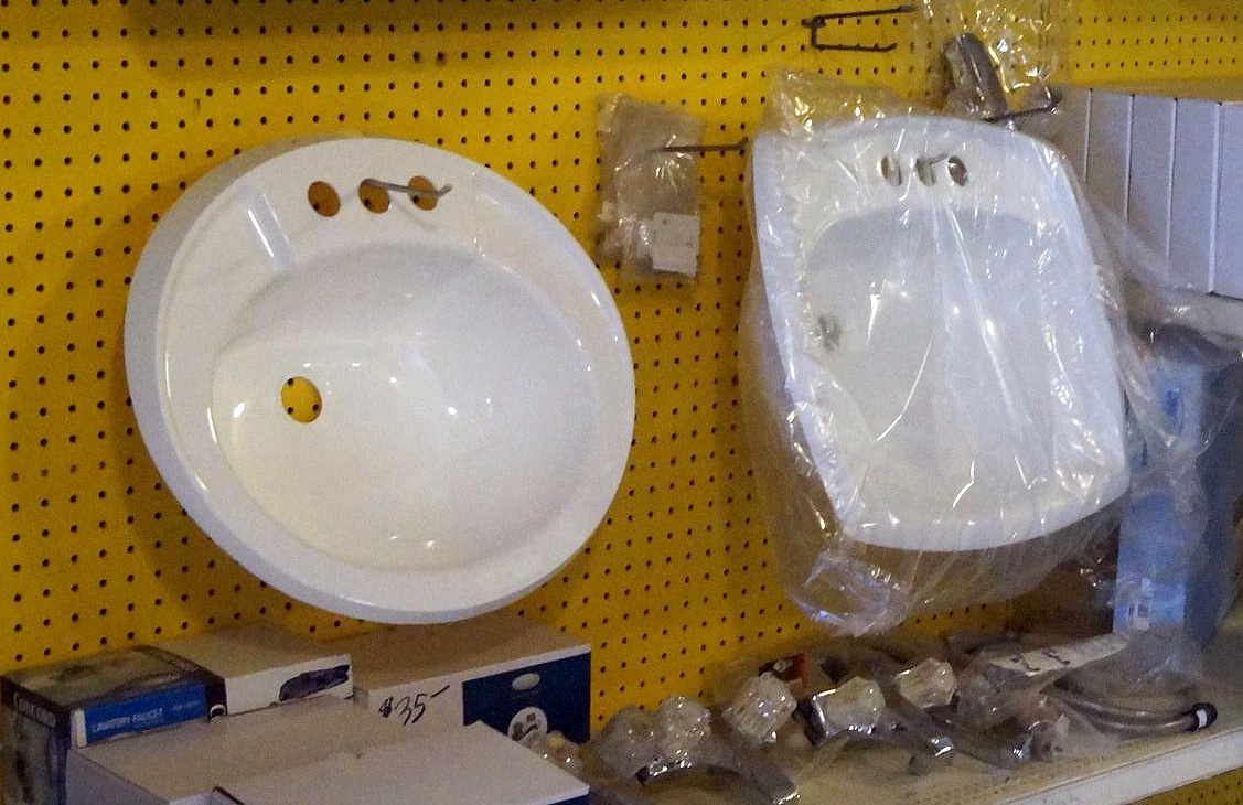 An oval and a rectangular ceramic bathroom sinks hang on a warehouse pegboard.