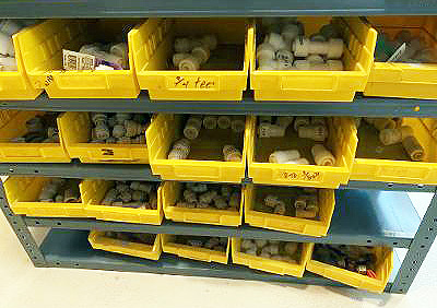 Pipe fittings in containers on warehouse shelves.